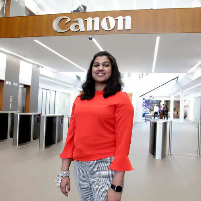 A woman in a bright red blouse and patterned pants stands in a modern Canon office, with the company