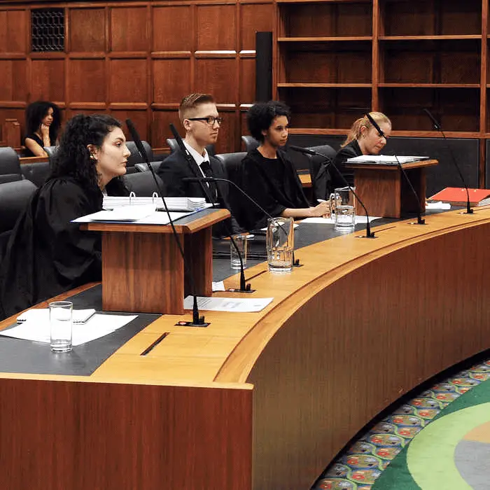 Group of students dressed in barister gowns sat behind a court desk