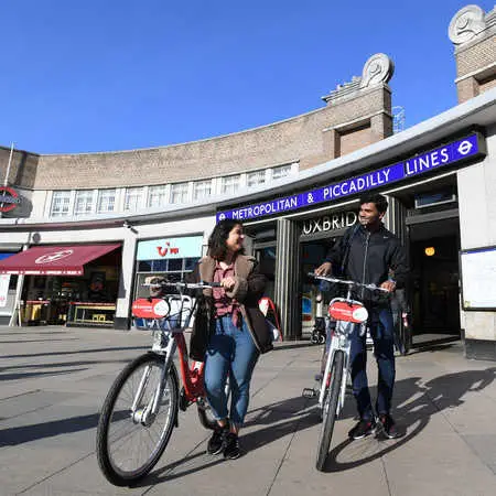 A man and a woman with Santander bikes outside of Uxbridge underground station.