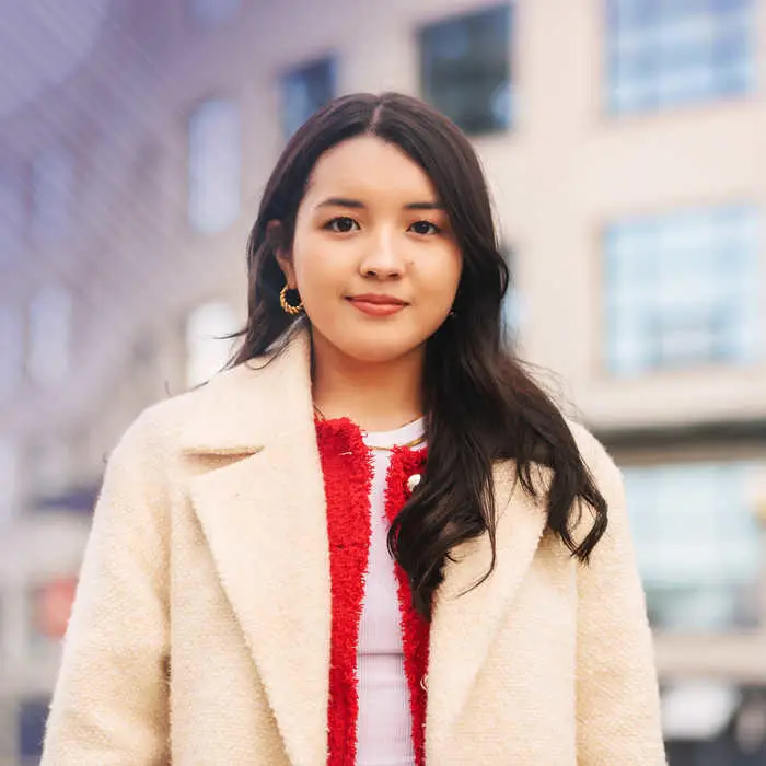 woman in a jacket in front of a building smiling into the camera