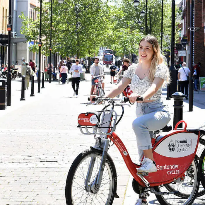 student on a bike with a brunel university sign